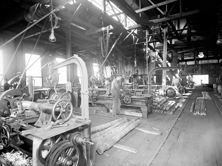 A machine shop around 1900: rows of lathes, each driven by a leather belt from shafts running along the ceiling.
